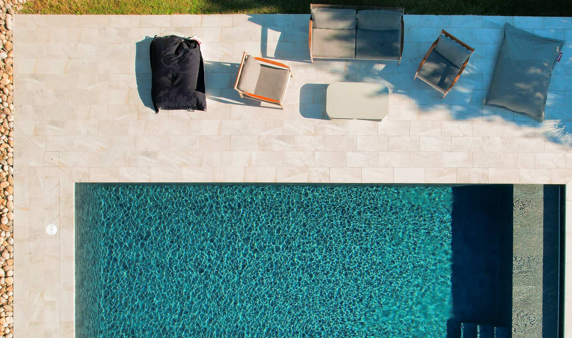 Vue aérienne d'une piscine avec terrasse carrelée blanche et mobilier de jardin réalisé par Aloha